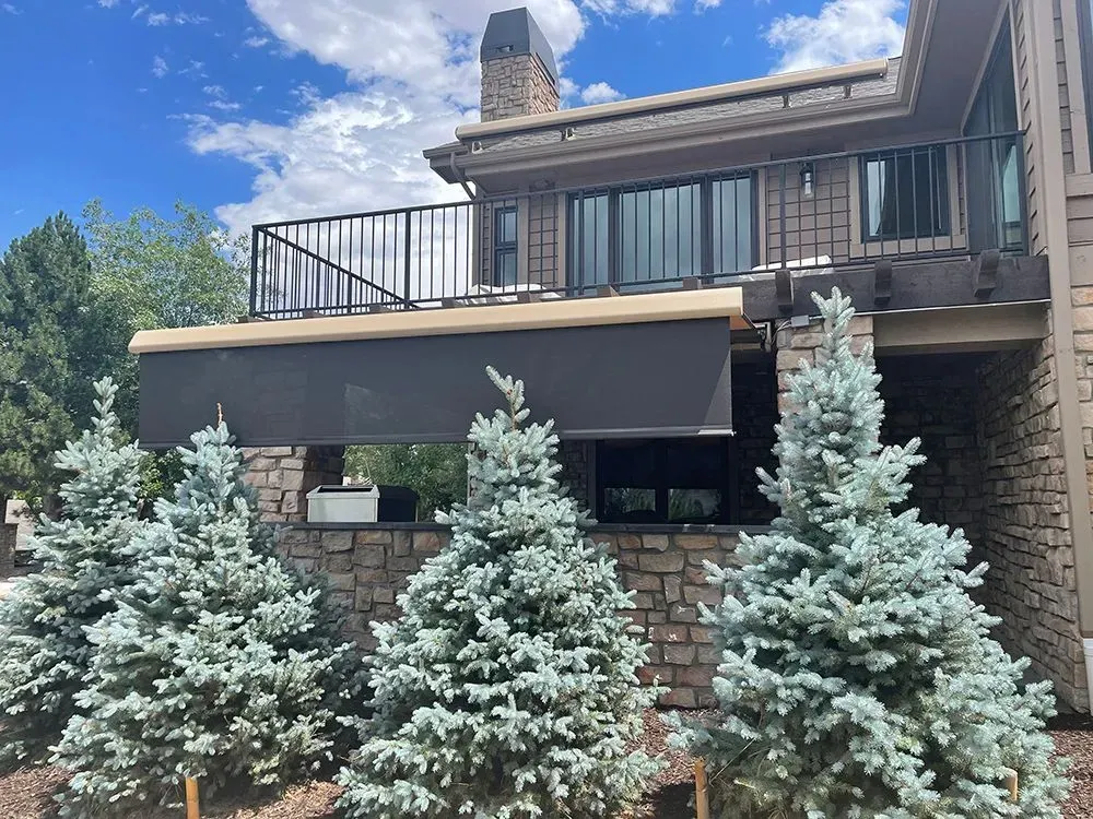 Modern house facade with a balcony, stone chimney, and row of evergreen shrubs in front