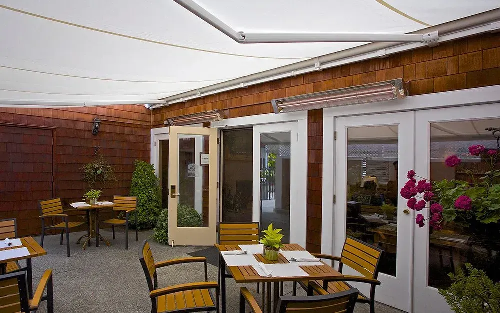 Outdoor patio with white tables, yellow chairs, brick wall, and potted flowers under a canopy