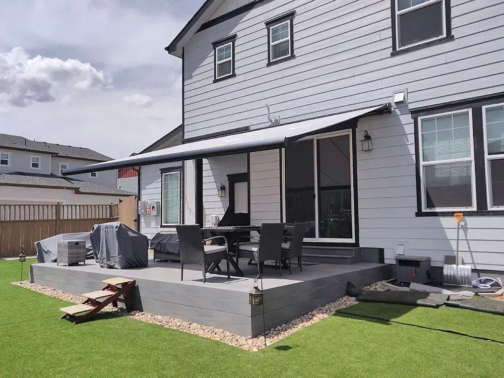 Backyard patio with gray deck, outdoor furniture, grill, and sliding doors on a house