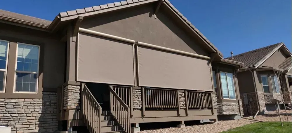 Beige apartment building with closed patio shades and a small wooden deck under a clear blue sky
