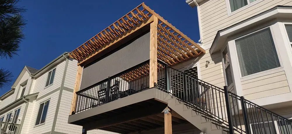 Outdoor staircase beside beige apartment buildings, with a wooden pergola on the top deck.