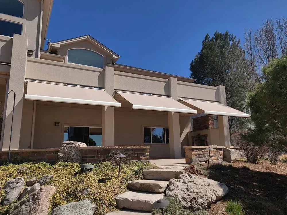 Two-story beige townhouse with stone steps, awnings, and desert landscaping under a clear blue sky