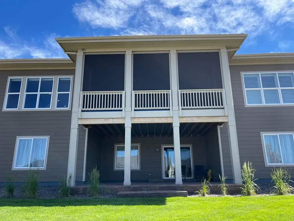 Back of a two-story home with a screened-in porch and windows; light blue sky and green grass visible.