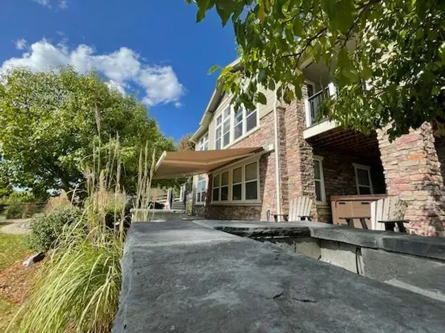 Tan retractable awning covers a patio next to a brick house under a blue sky.