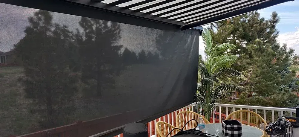 Outdoor patio with dark shade screen, deck railing, and trees visible through the shade.