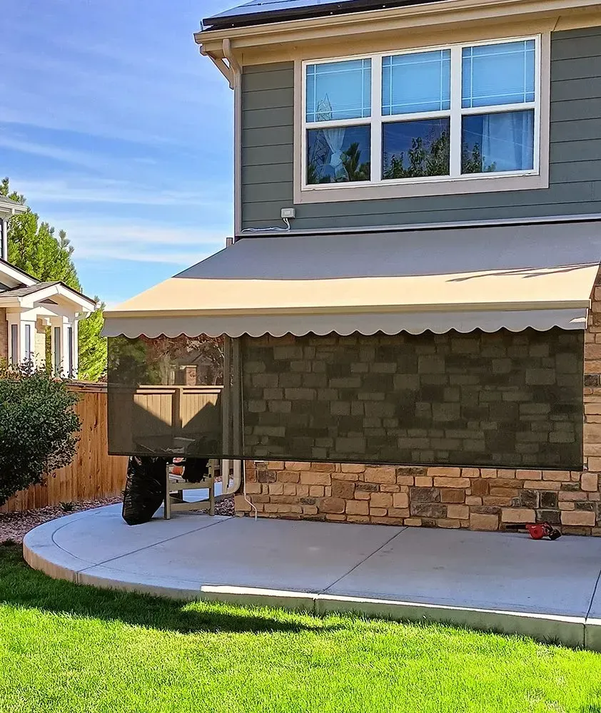 A beige awning shades a patio next to a house with a green exterior.