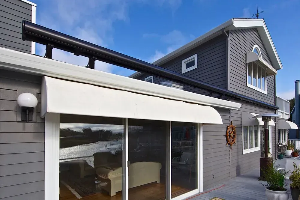 Gray house with white awnings over glass doors, blue sky background.