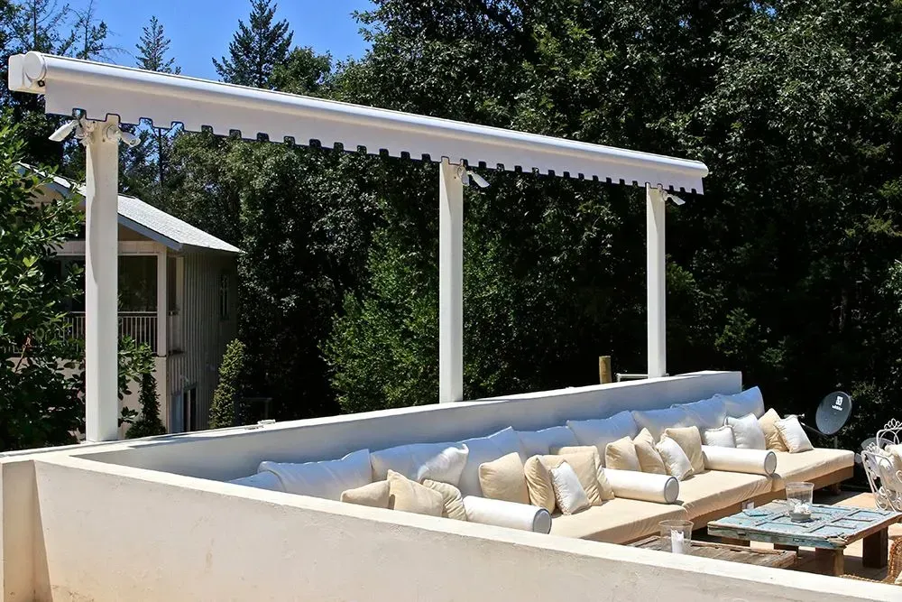 White awning over a built-in outdoor seating area with pillows. Trees and a building are in the background.