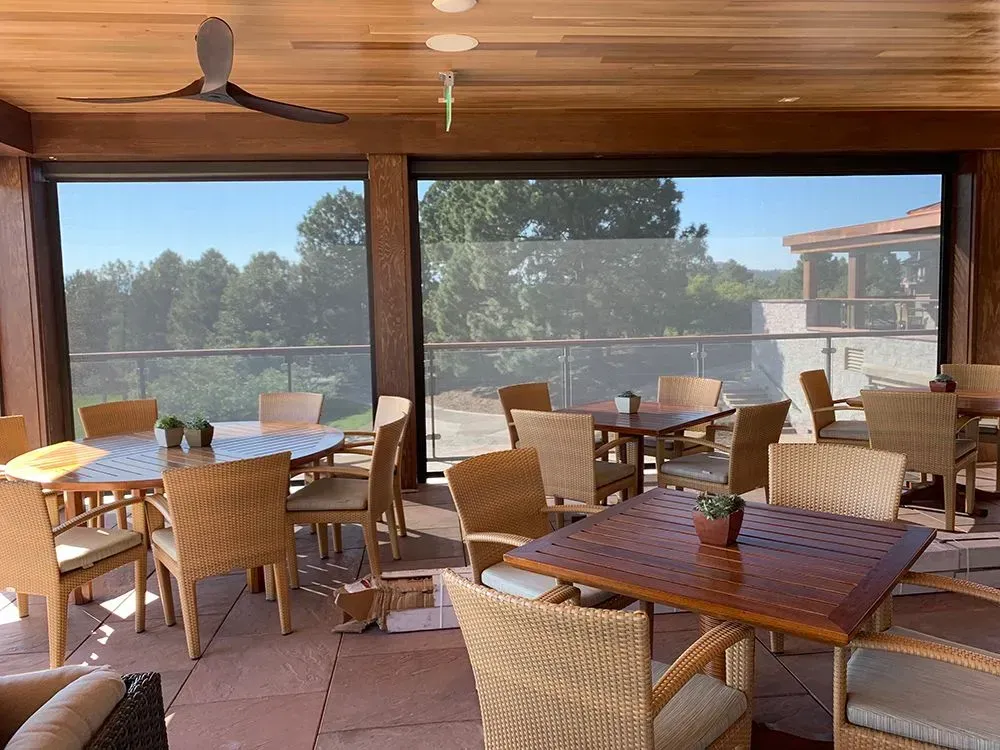 Outdoor dining area with tables and chairs, partial sun screen, and a view of trees.