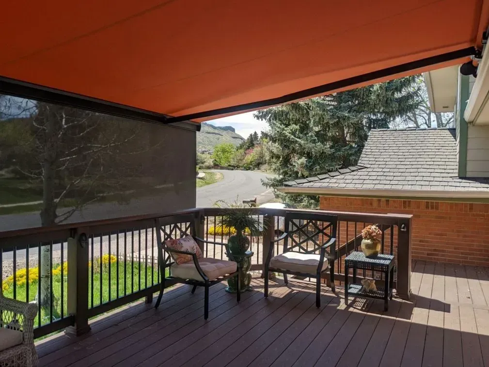 Deck with orange awning, chairs, and shade screen. Brown railings and deck, trees and road in the distance.