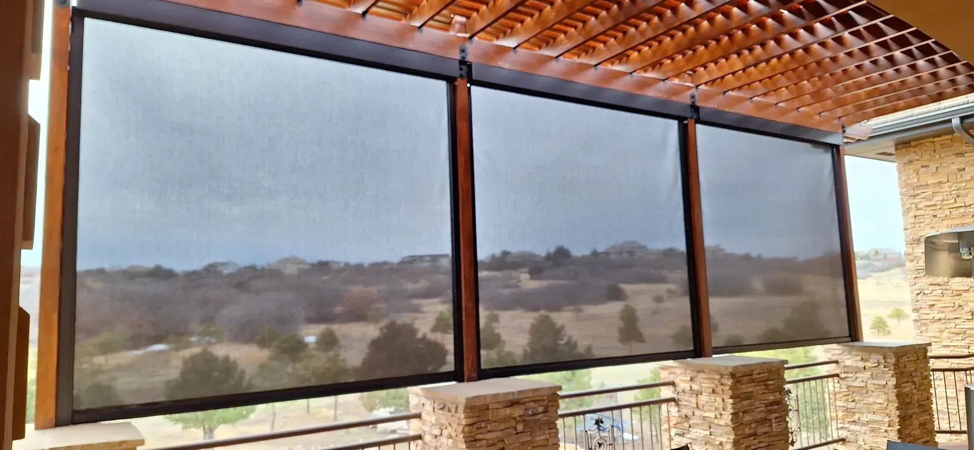 Outdoor patio with mesh screens overlooking a landscape, under a wooden pergola.