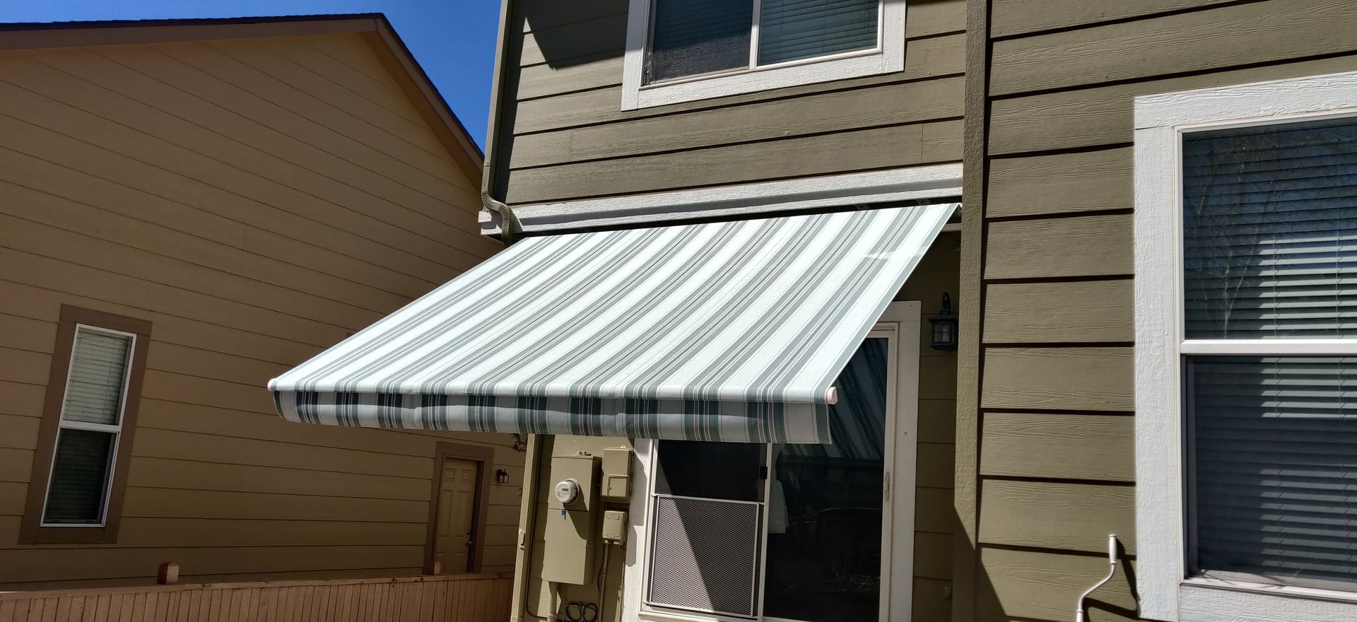 A house with a striped awning over the front door. The house has green siding.
