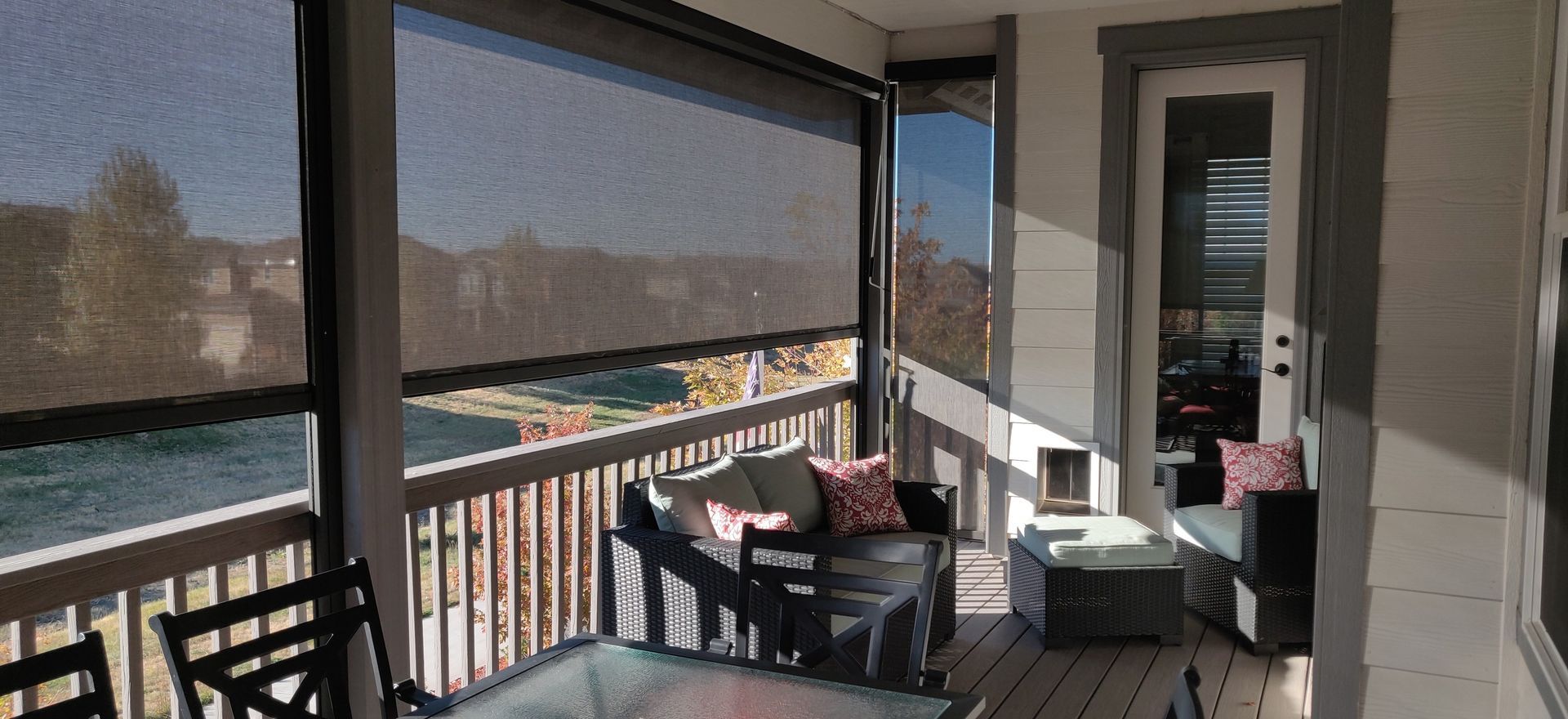 Screened porch with retractable shades, outdoor furniture, and a view of trees and sky.