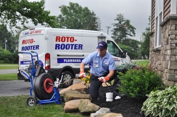 A man is kneeling in front of a roto-rooter van