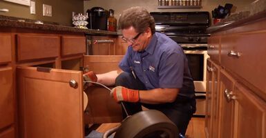 A plumber is fixing a sink in a kitchen.