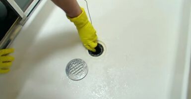 A person wearing yellow gloves is cleaning a shower drain.