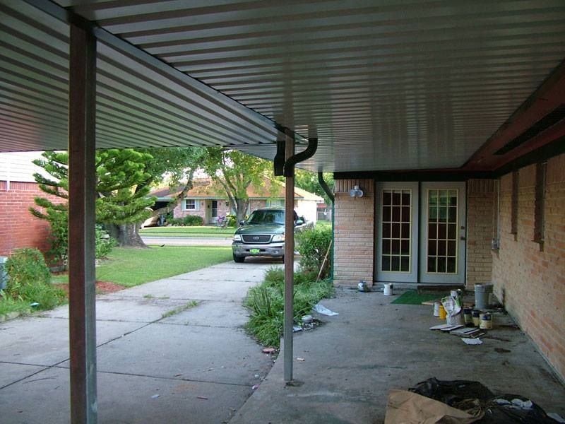 A car is parked under a covered porch in front of a house