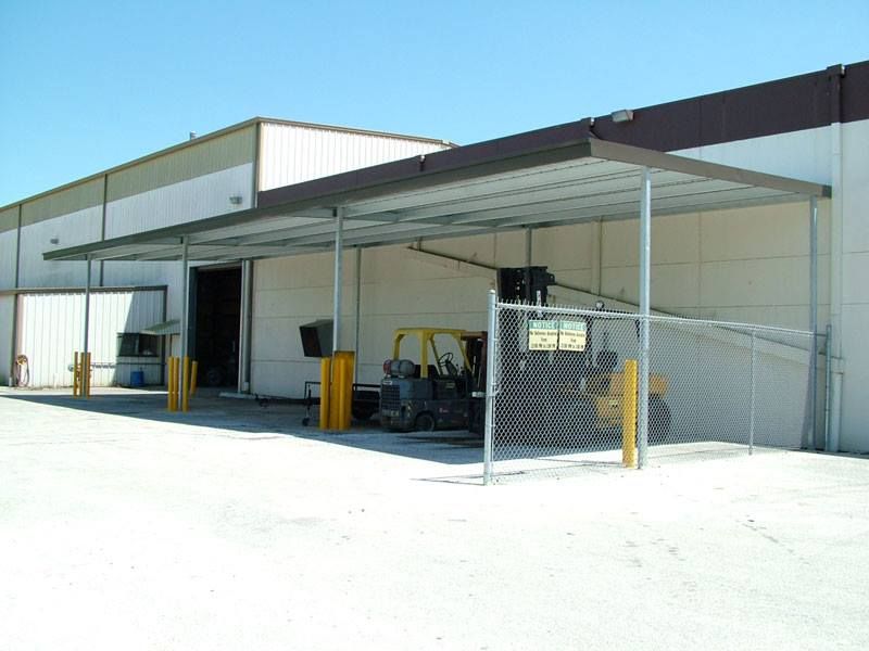 A forklift is parked under a canopy in front of a building