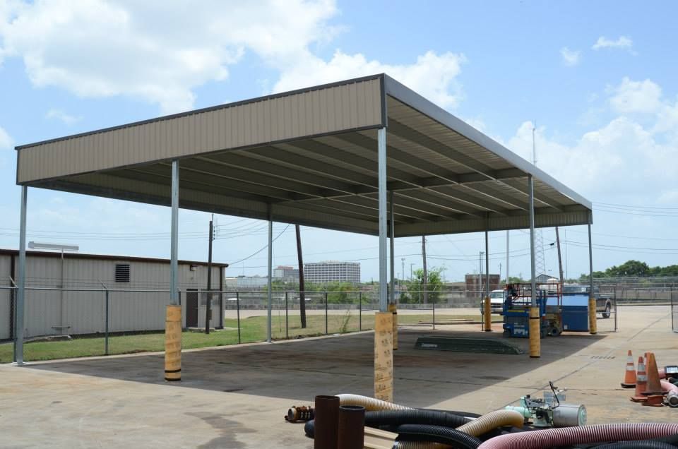 A covered parking lot with a fence and a building in the background