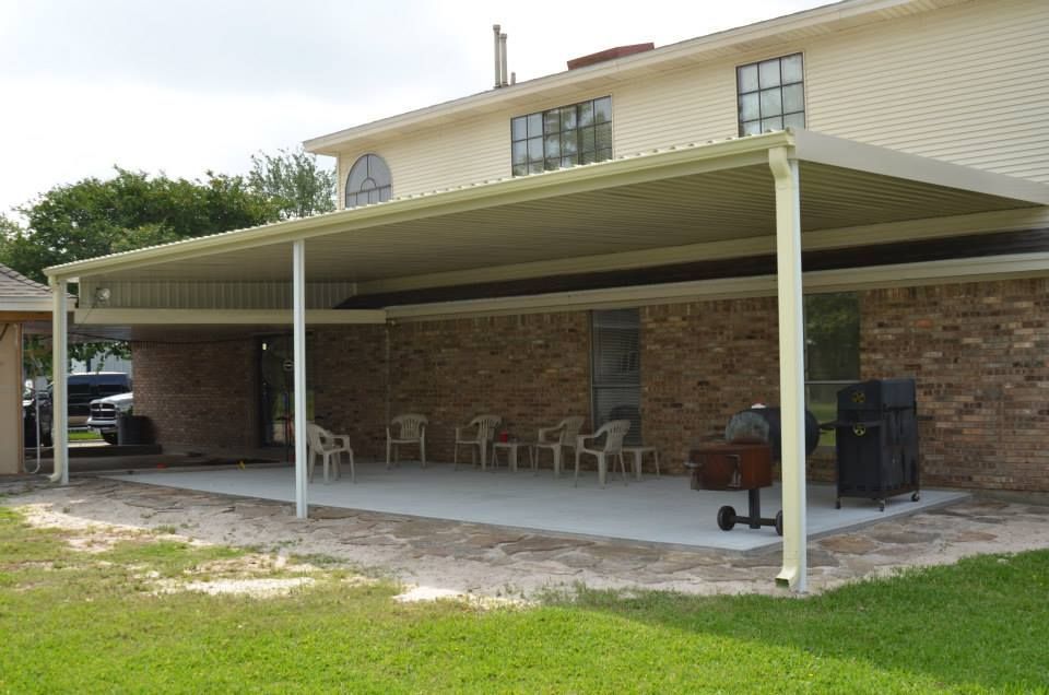 A large covered patio with chairs and a grill in front of a brick house.