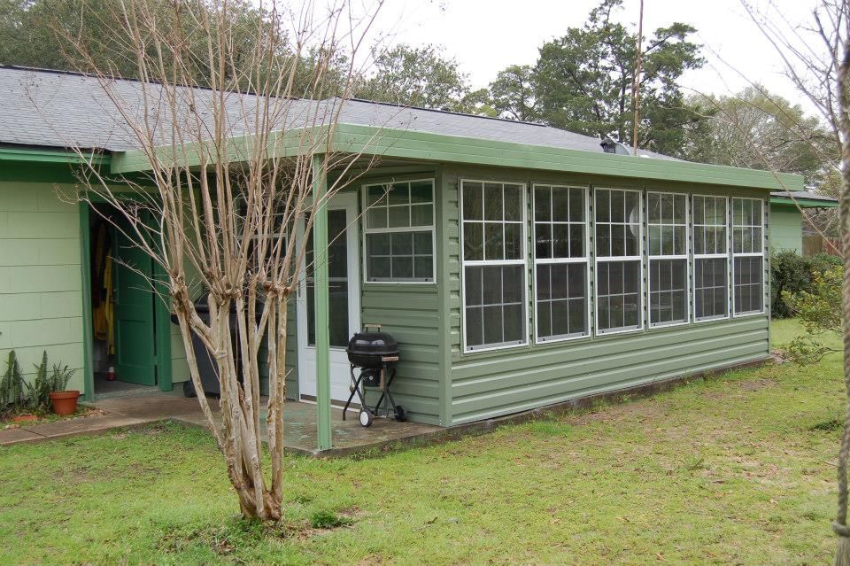 A green house with a screened in porch and a grill