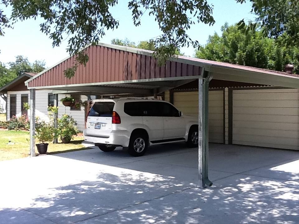 A white suv is parked under a carport in front of a house.