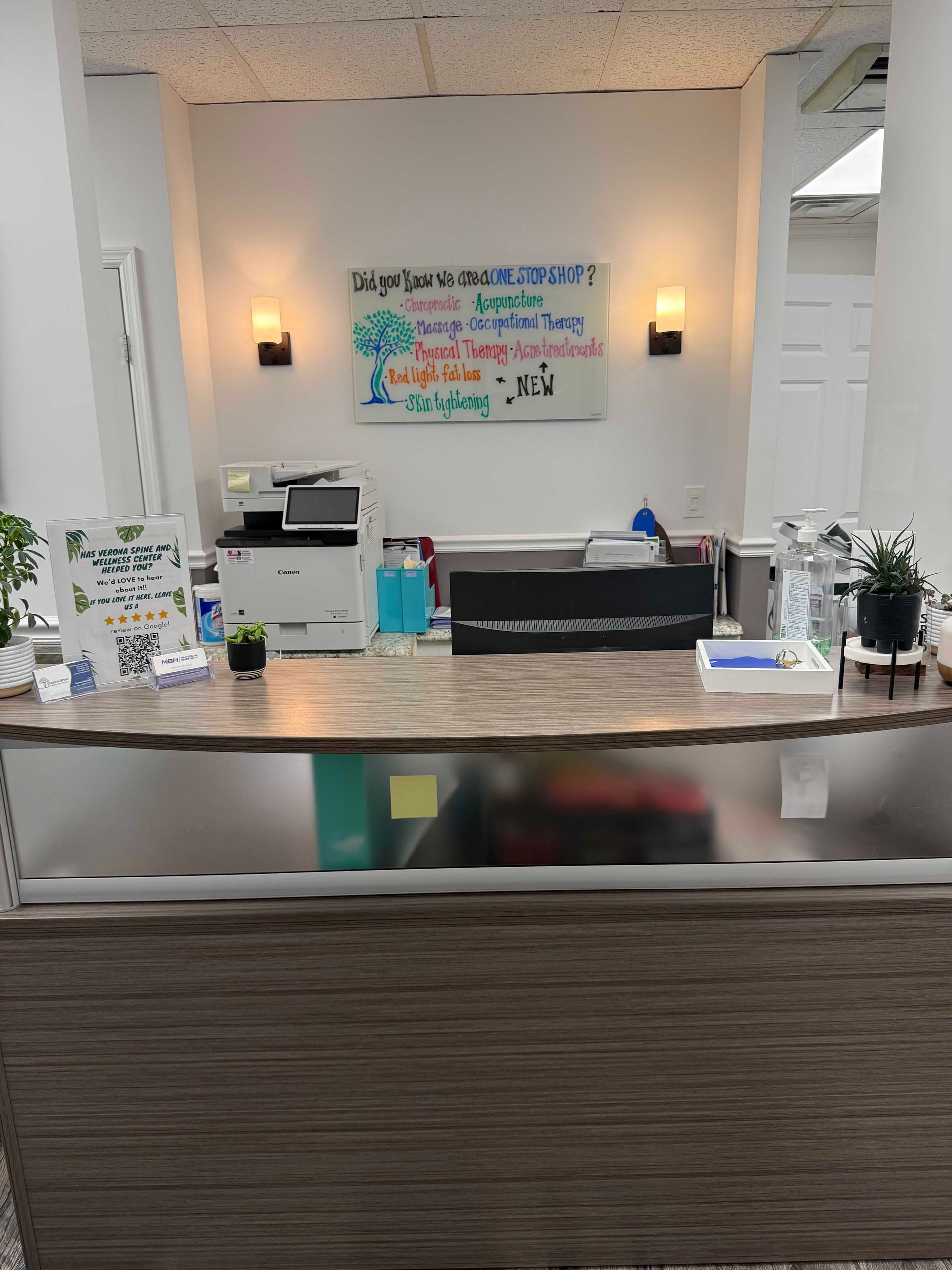 Reception desk in a bright office lobby with wall sign, flowers, and office equipment