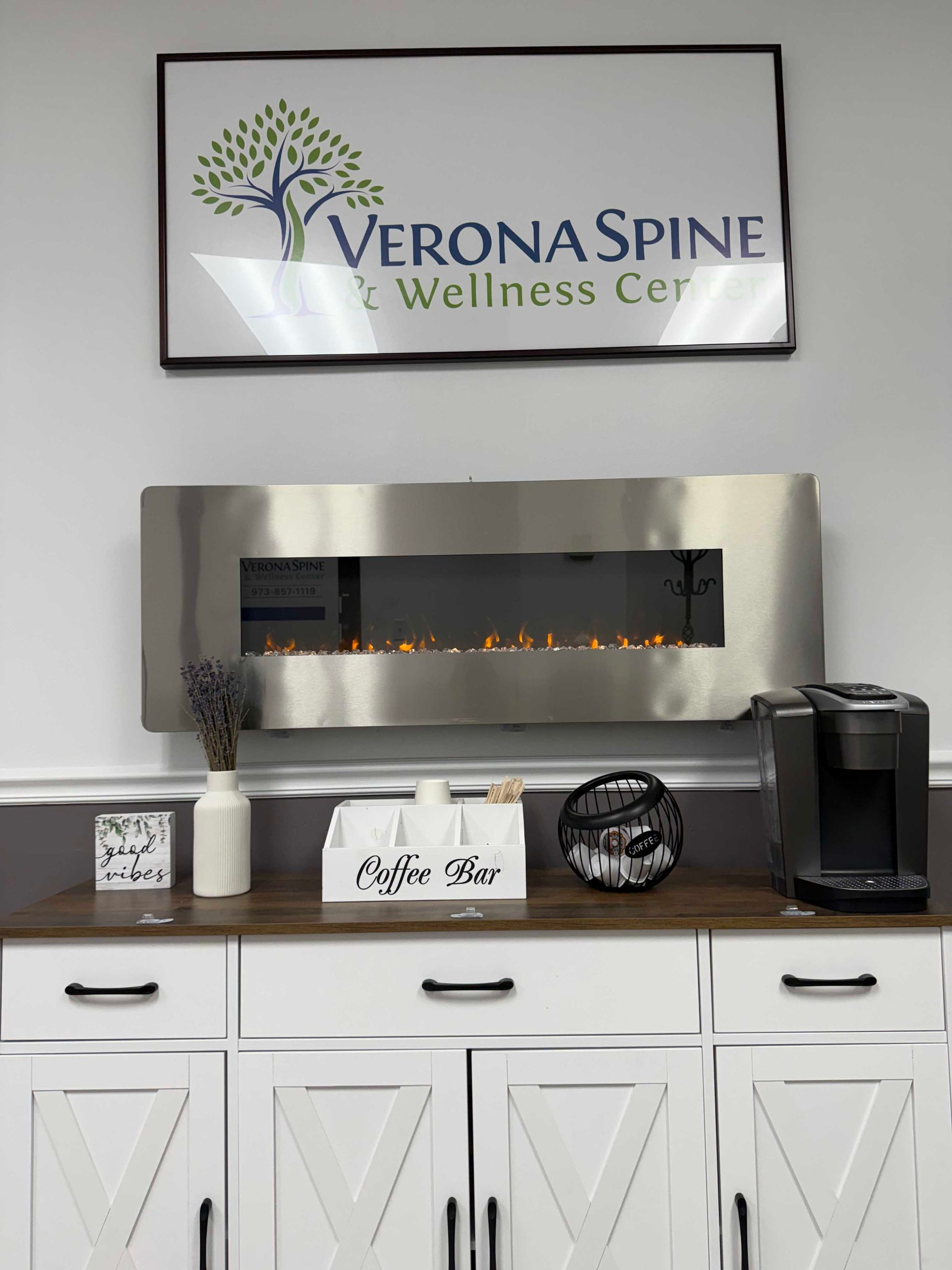 Verona Spine Wellness Center sign above a wall fireplace and white cabinets in a lobby
