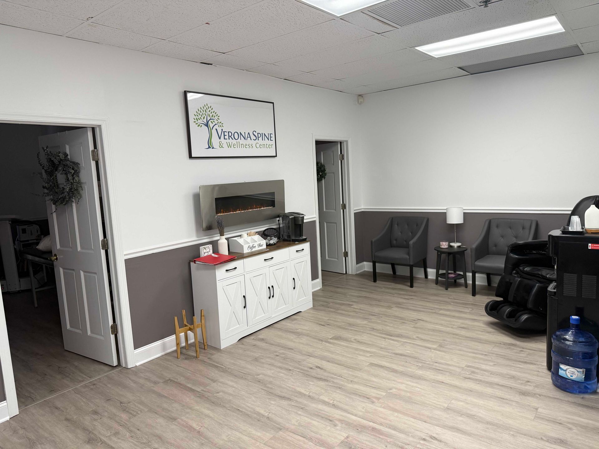Empty office waiting area with chairs, white cabinets, wall art, and a water cooler on the right.