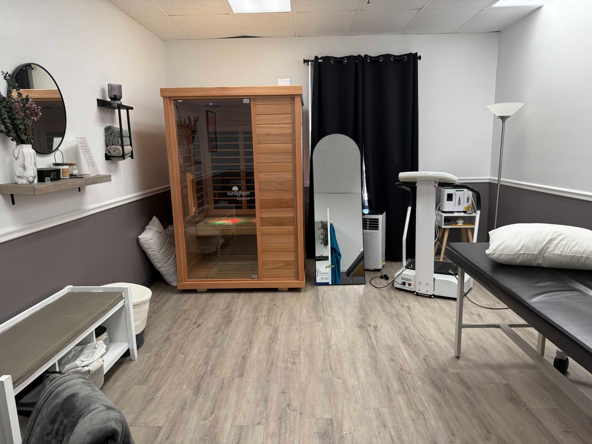Clinical room with treatment table, massage chair, wooden cabinet, mirror, and floor lamp