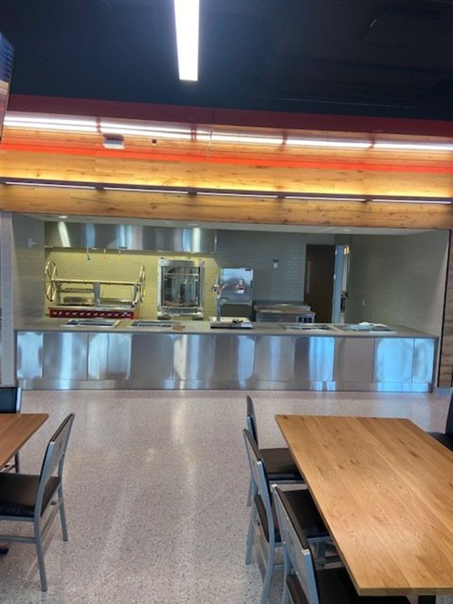 A dining room with tables and chairs and a kitchen in the background
