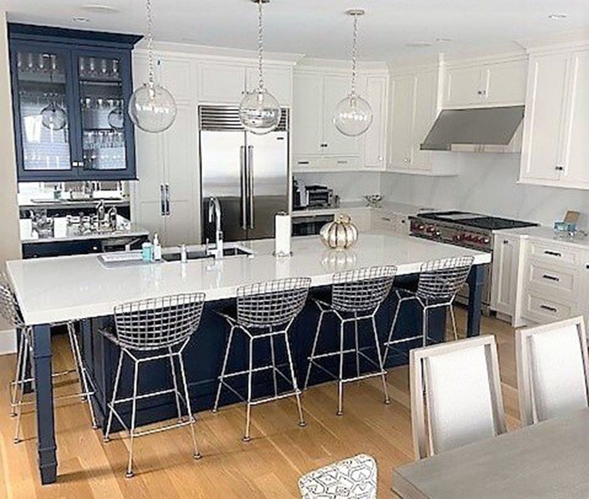 A kitchen with a large island, stools, a table and a refrigerator