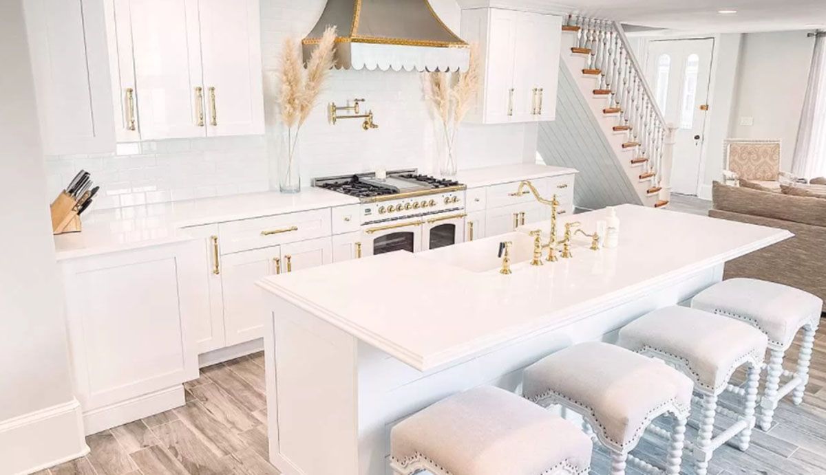 A kitchen with white cabinets, a stove, sink, and stools