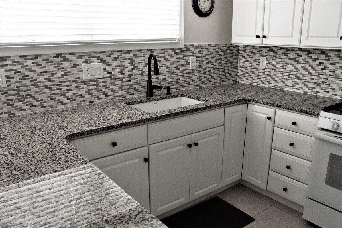 A kitchen with granite countertops, white cabinets, a stove, and a sink