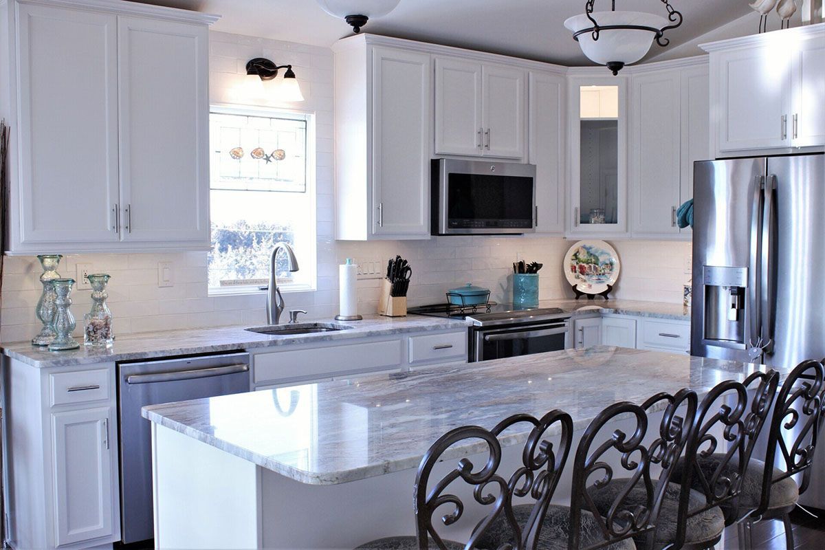 A kitchen with white cabinets, stainless steel appliances, granite countertops, and a large island