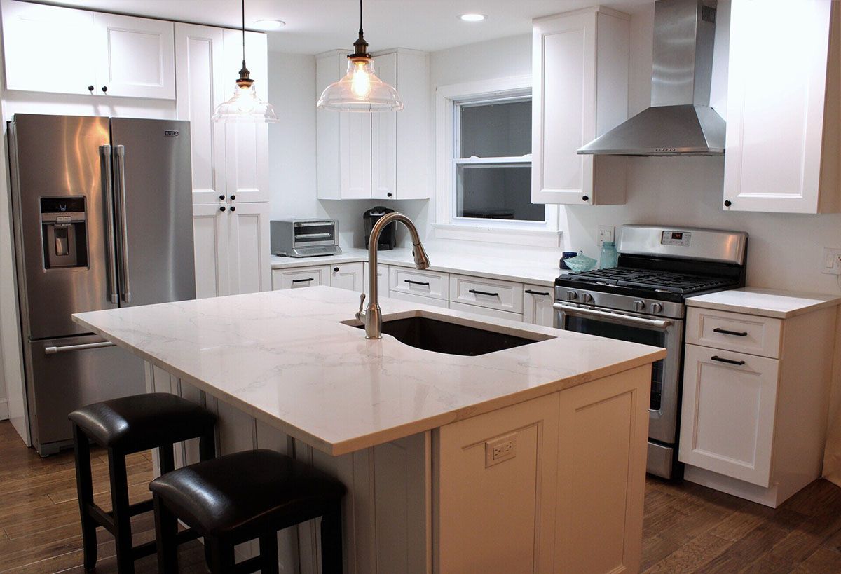 A kitchen with white cabinets, stainless steel appliances, a large island, and a sink