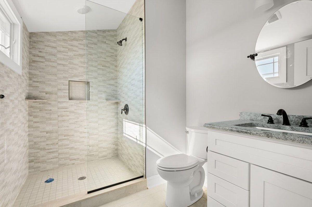 A bathroom with a toilet, sink, mirror, and walk-in shower