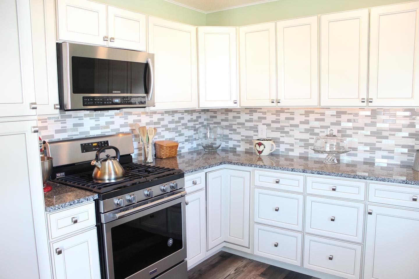 A kitchen with white cabinets , stainless steel appliances , granite counter tops and a stove top oven.