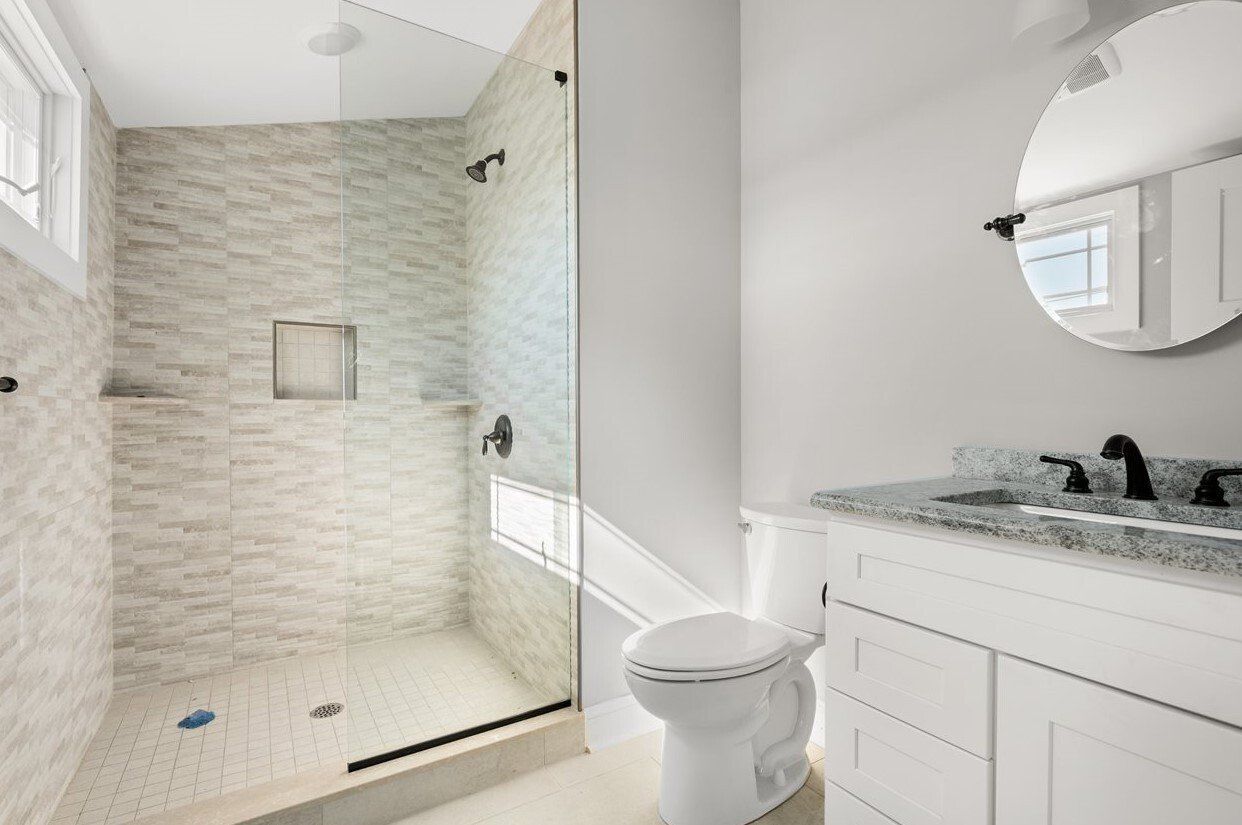 A bathroom with a toilet , sink , mirror and walk in shower.