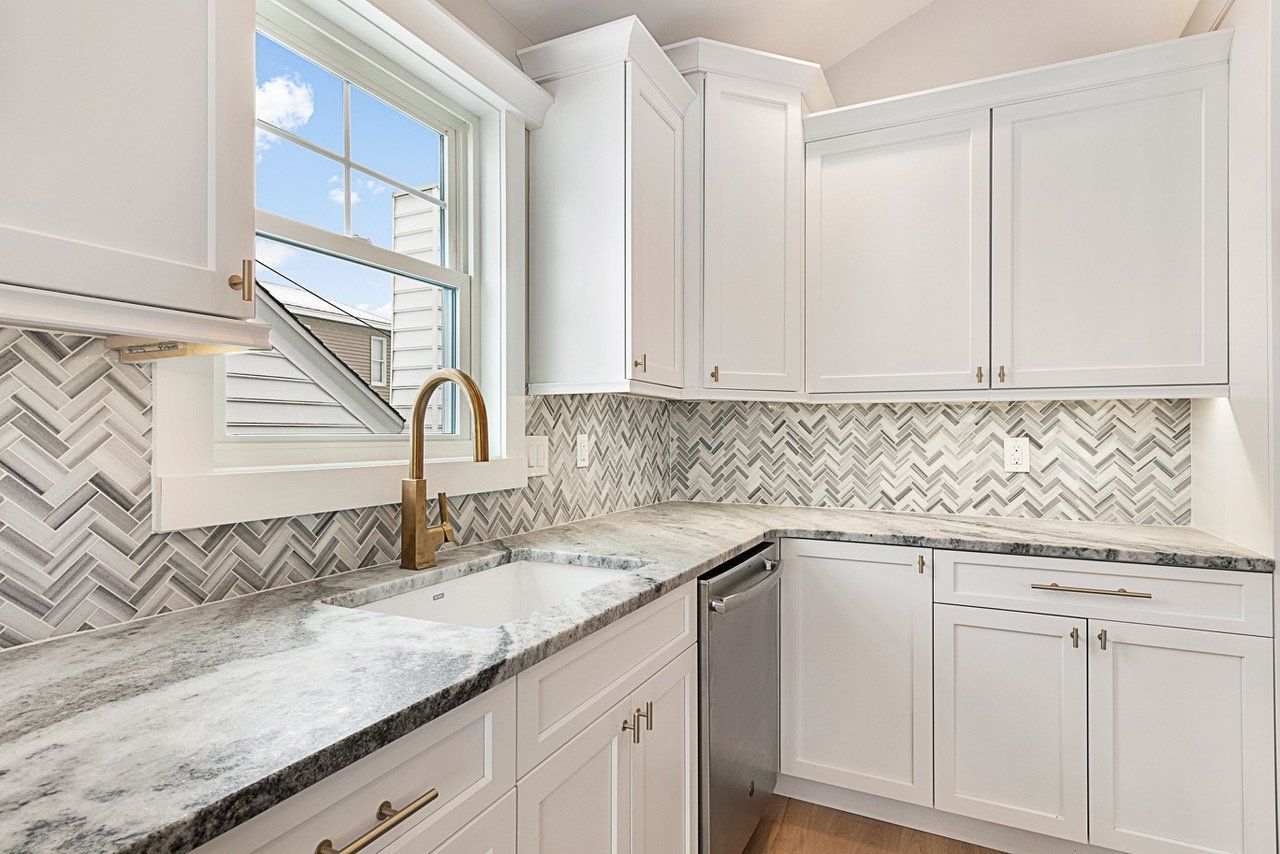 A kitchen with white cabinets , granite counter tops , a sink and a window.
