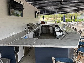 A large outdoor bar with a marble counter top and a flat screen tv.