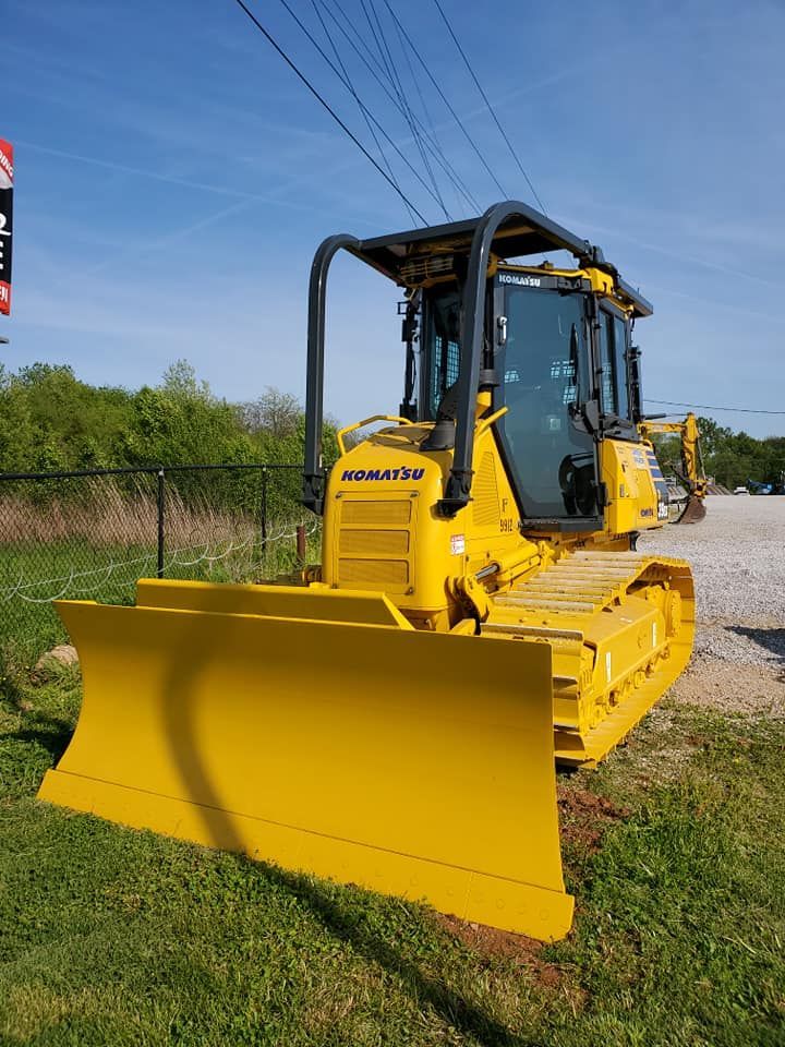 A yellow bulldozer is parked in the grass next to a dirt road.