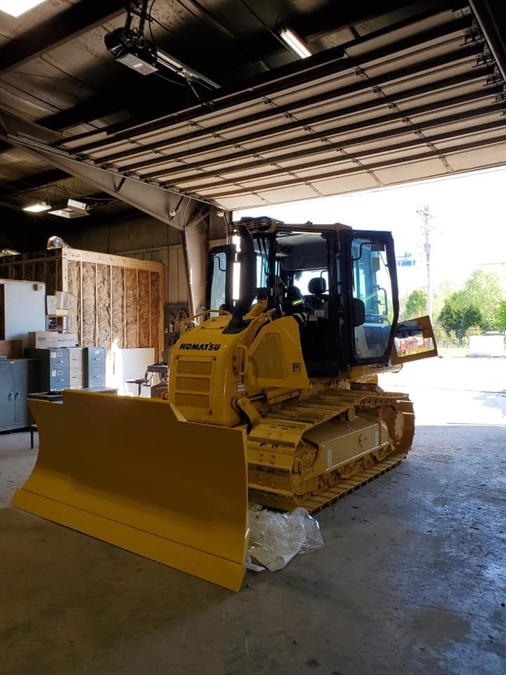 A yellow bulldozer is parked in a garage with the door open.