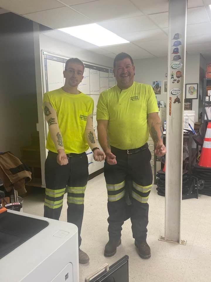 Two men in neon yellow shirts are standing next to each other in a room.