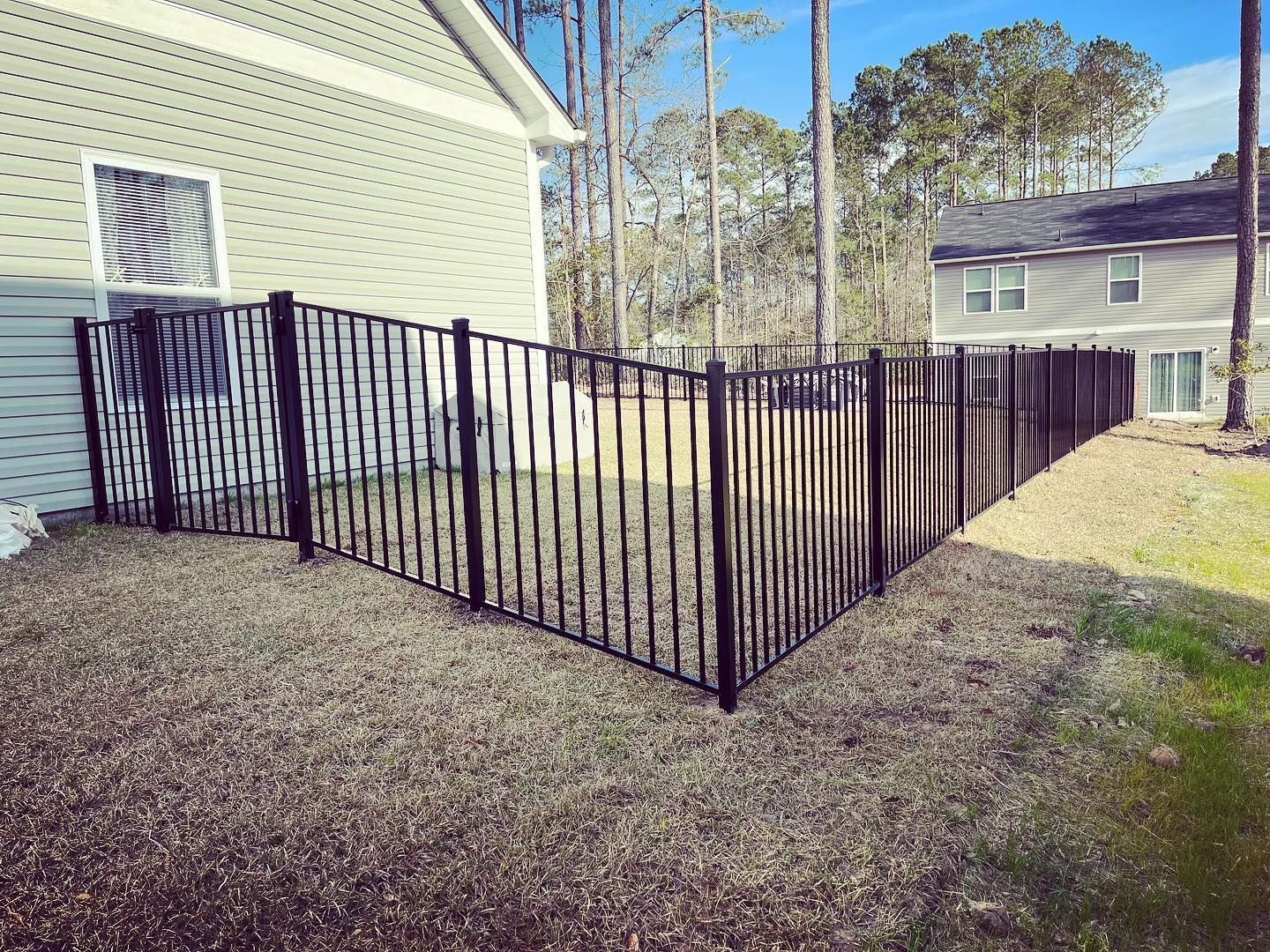 A black fence is surrounding a yard in front of a house.