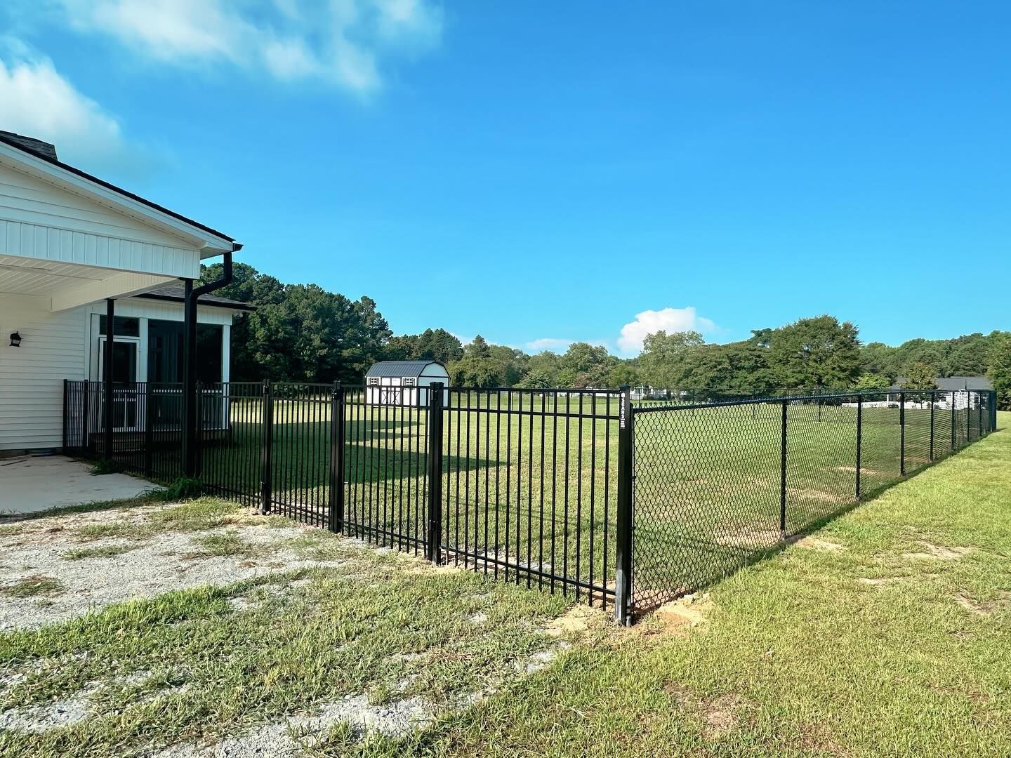 A black chain link fence surrounds a grassy field in front of a house.