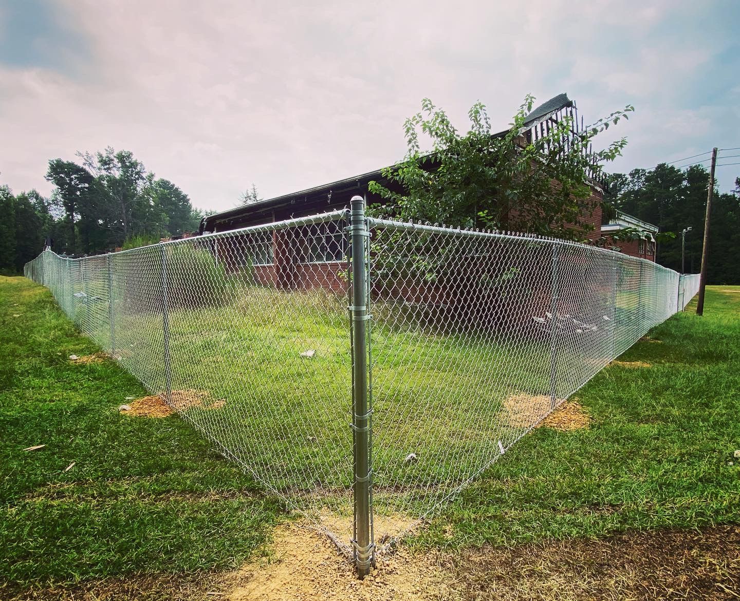 A chain link fence is surrounding a grassy field with a house in the background.