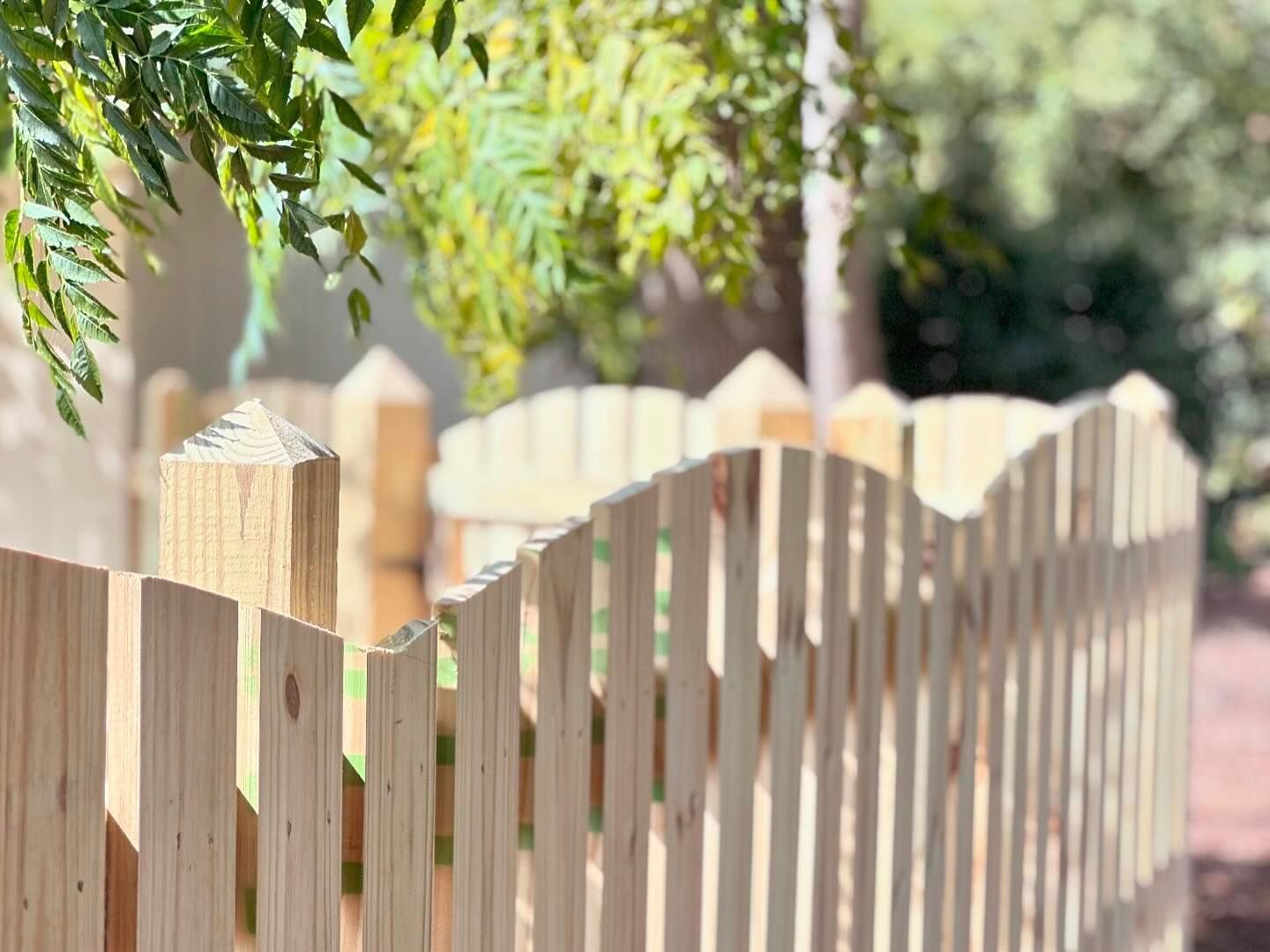 A close up of a wooden picket fence with trees in the background.
