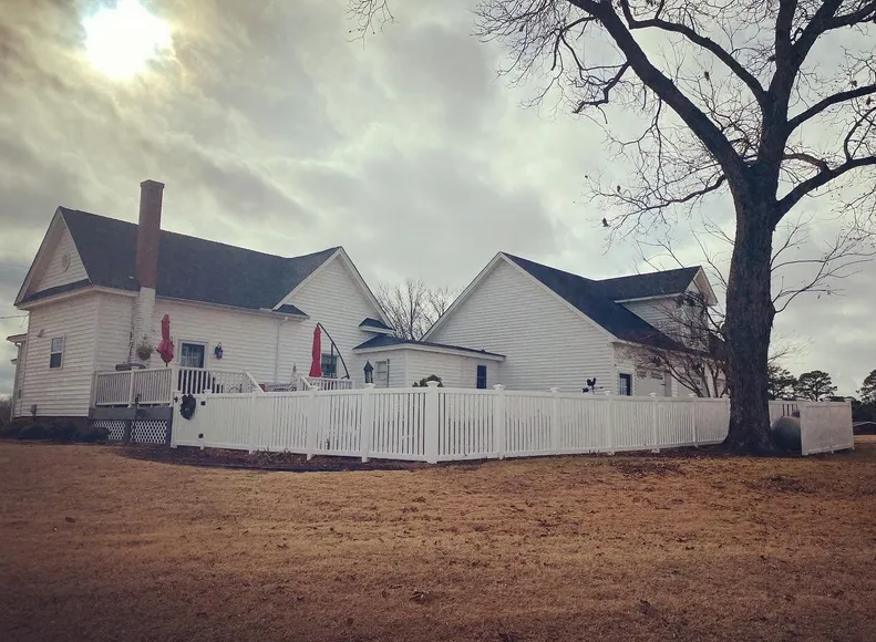 A white house with a white fence and a tree in front of it.
