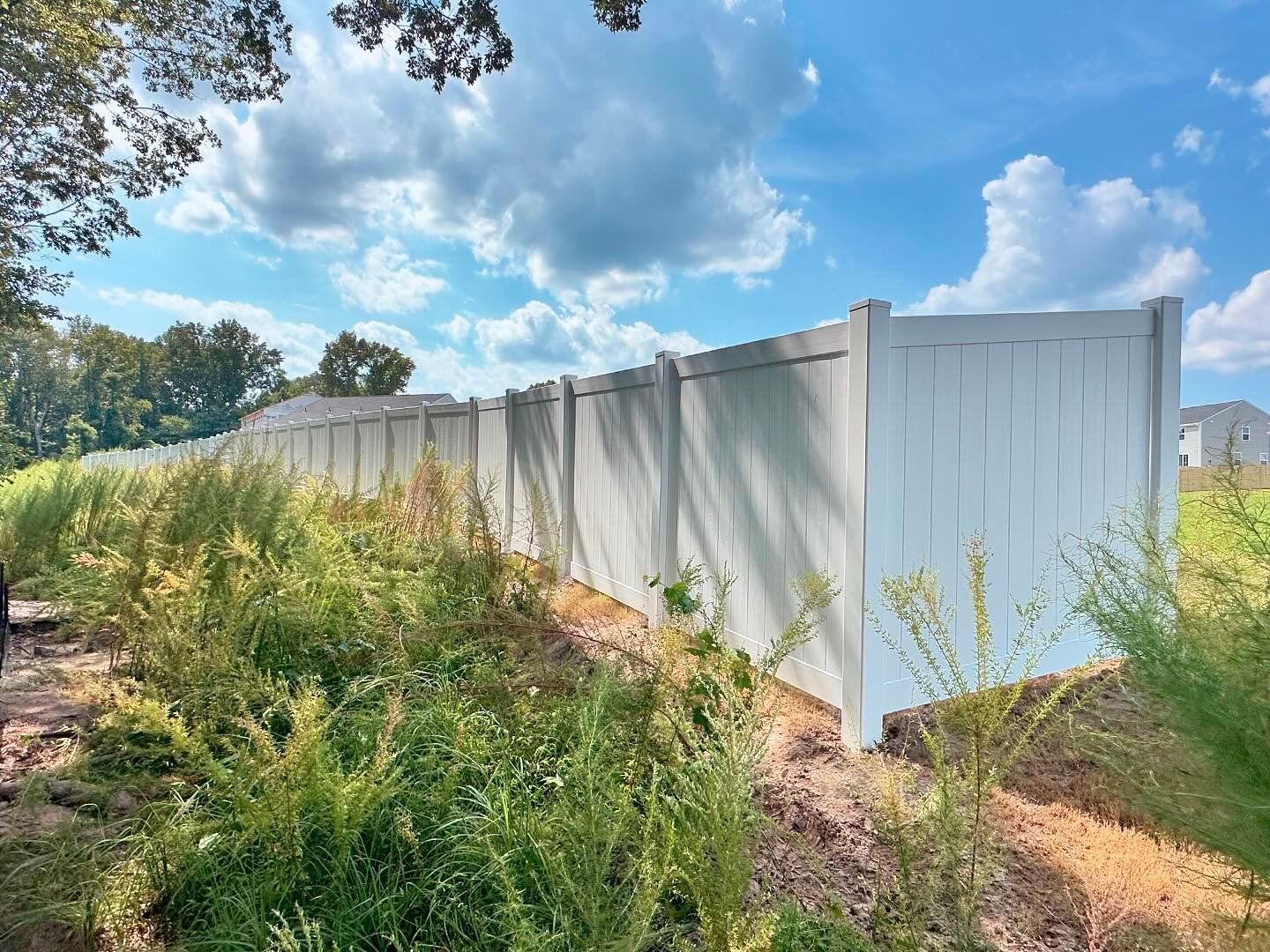 A white fence is surrounded by tall grass and trees.